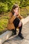 Teenage girl on the street sits on the edge of the road, sidewalk with a glass of coffee in her hand.