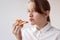 A teenage girl in a white shirt has taken a bite of pizza and is holding it in her mouth