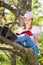 Teenage girl in white T-shirt and pink hat is sitting on a tree in the garden, smiling and reading interesting book. Great idea