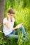 Teenage girl in white T-shirt sitting on the grass by the tree in the garden and reading interesting book. Great idea and activity