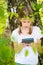 Teenage girl in white T-shirt standing by the tree in the forest and reading book on ebook reader. Great idea and activity to