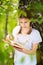 Teenage girl in white T-shirt standing by the tree in the forest and reading interesting book. Great idea and activity to spend