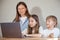 teenage girl works on a laptop, her mother helps her , and her younger brother