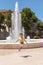 Teenage girl in a yellow T-shirt jumps on the street near the fountain