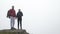 Teenage hiking couple in love kissing on the top of foggy mountain admiring the nature -