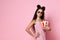 Teenage kid in striped dress and aviator sunglasses. She is holding pack of popcorn, posing on pink studio background. Close up