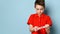 Teenage male dressed in red t-shirt. He holding crumpled hundred dollar bill, looking disappointed, posing on blue background