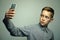 Teenage serious boy with stylish haircut taking selfie on smartphone