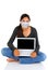 Teenage student sitting with her legs crossed with open laptop computer in her lap., wearing a COVID-19 protective mask