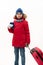 Teenage traveler boy wearing red parka and blue denim jeans walks with a boarding pass and suitcase on white background