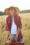 Teenage traveler in farm ripe oat field with old-fashioned brown suitcase looking at camera