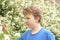 Teenager with allergies standing in a blue t-shirt among the Jasmine bushes and suffers from bad health