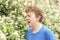 Teenager with allergies standing in a blue t-shirt among the Jasmine bushes and suffers from bad health