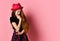 Teenager in black dress, checkered shirt on waist, red hat. She thought, touching her face, posing on pink background. Close up