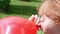 Teenager boy is blowing air balloon. Handsome redhead boy inflating red heart shaped balloon holding balloon in hands