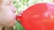 Teenager boy is blowing air balloon. Handsome redhead boy inflating red heart shaped balloon holding balloon in hands