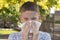 Teenager boy blows his nose in a paper handkerchief on a background of vegetation in a park. Sneezes