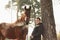 Teenager boy and brown horse standing near the tree