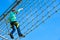 Teenager boy moves the vertical grid on the obstacle course in the amusement park, outdoor activities, rock climbing, danger, trai