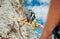 Teenager boy on the natural cliff climbing wall. Boy hanging on a rope using a climbing harness and the father belaying him on the