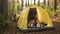 Teenager boy playing music on guitar inside camping tent in sunny forest. Boy and girl teenagers singing song with