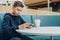 Teenager boy sits at table in cafe, drinks milkshake, uses smartphone. Boy plays games on smartphone, browsing internet.