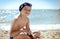 A teenager boy smiles and sitting on the sand in swimming trunks . The concept of relaxation and tranquility. Copy space on the