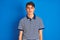 Teenager boy wearing casual t-shirt standing over blue  background looking sleepy and tired, exhausted for fatigue and