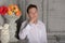 Teenager boy in a white shirt and pants leaning on a marble fireplace shelf next to a vase of flowers