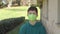 Teenager in a bright green protective medical mask in the countryside in the yard of the house.