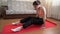 Teenager brunette slim girl in face mask in pink sport bra, black pants, white socks doing yoga poses on red mat at home