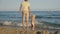 Teenager and child having fun on the beach. Two years old blond baby girl standing knee-deep in sea water and splashing