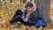 A teenager communicates on a smartphone sitting by a tree in the autumn forest