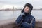 Teenager dressed warm jacket and hat with earflaps thinking, Peter and Paul fortress is on a background, granite bridge across