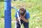 A teenager drinks water from a public column on the street. He scoops water with his hands.