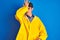 Teenager fisherman boy wearing yellow raincoat over  background surprised with hand on head for mistake, remember error