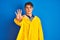 Teenager fisherman boy wearing yellow raincoat over isolated background doing stop sing with palm of the hand