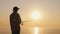 A teenager is fishing on the shore of a beautiful lake at sunset. Ahead is visible only to the vast water