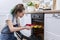 Teenager girl in an apron with preparing cupcakes, putting tray in oven