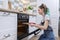 Teenager girl in an apron with preparing cupcakes, putting tray in oven