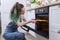 Teenager girl in an apron with preparing cupcakes, putting tray in oven