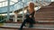 Teenager girl in black leather jacket sitting on stairs on urban landscape. Stylish girl in black leather jacket sitting