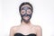 Teenager girl in a black mask, natural photo of a real mask on a young girl. Texture dark cream. Model on a white background