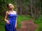 Teenager girl in a blue high fashion dress posing on a footpath in a forest. Senior prom pictures. Glamour and elegance concept.