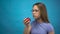 Teenager girl with braces on her teeth eats a red apple on a blue background. Girl with colored braces bites off an