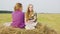 Teenager girl friends sitting on hay stack at farming field in village. Carefree girls talking on hay stack at