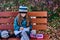 A teenager girl in glasses, a coat and a knitted hat sits on a bench in the park and draws a drawing on paper.