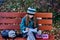 A teenager girl in glasses, a coat and a knitted hat sits on a bench in the park and draws a drawing on paper.