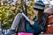 A teenager girl in glasses, a coat and a knitted hat sits on a bench in the park and draws a drawing on paper. Close-up.