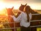 Teenager girl looking at dark horses by a metal gate to a field at stunning sunset. Warm sunshine glow. Selective focus. Light and